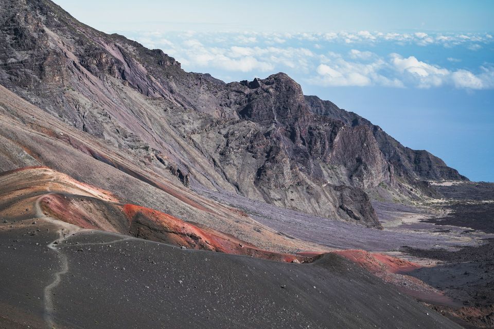 Red and grey cinder slopes with a thin trail winding down into a volcanic valley
