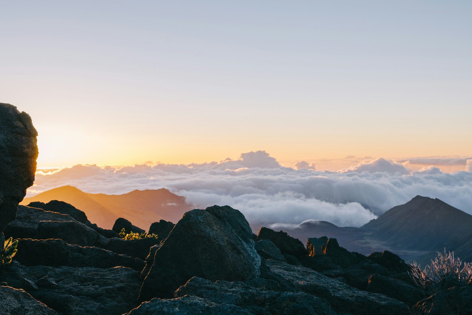 The sun rising above a sea of cloud, dark cinder cones and lava rock in the foreground
