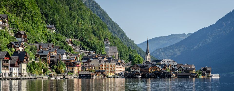 Boathouses and stacked houses along the shore below two church towers and a wooded mountainside