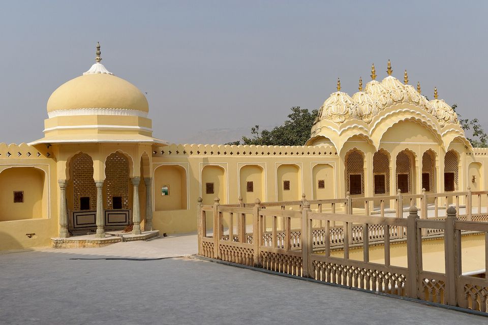 A pale yellow domed pavilion and a lobed-arch colonnade around a grey paved terrace with a stone balustrade, under a hazy grey sky
