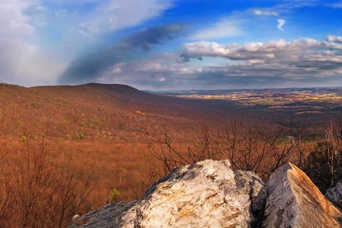 Boulders in front of rust-brown forest rolling to farmland under streaked cloud