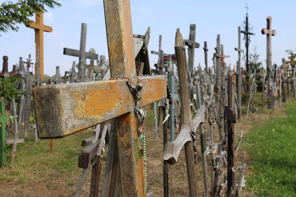 Close view of a worn ochre wooden cross hung with a beaded rosary and a small metal crucifix, rows of grey crosses fading into the distance