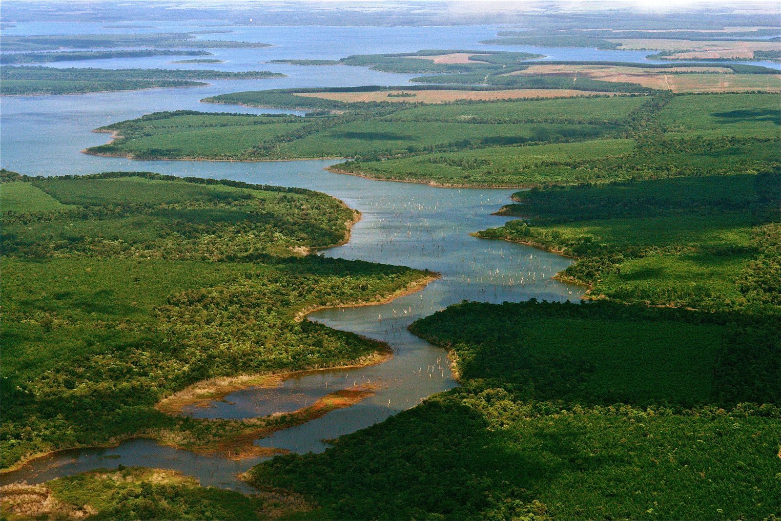 Aerial view of a winding channel of open water threading between islands of floating vegetation and green marsh, lagoons to the horizon