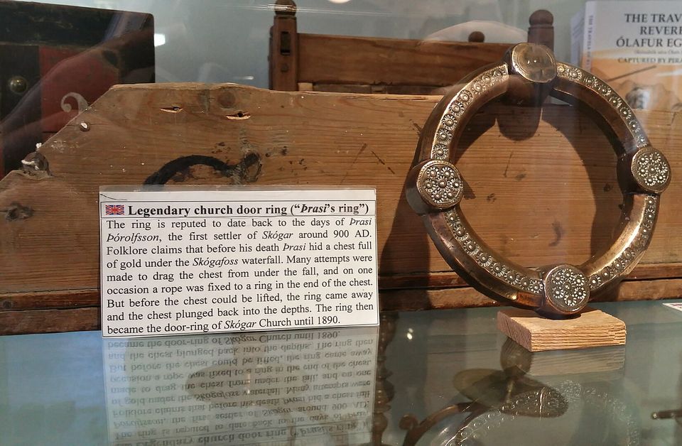 A bronze ring set with four round bosses, mounted on a carved wooden board in a glass case beside its museum label