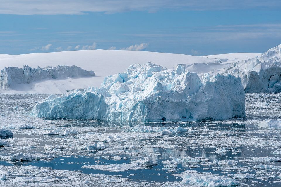 A large blue-white iceberg with fractured faces among smaller ice pieces on grey-blue water