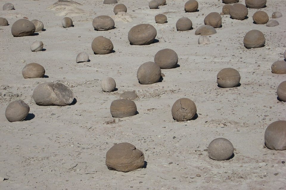 Dozens of grey stone balls scattered on pale ground