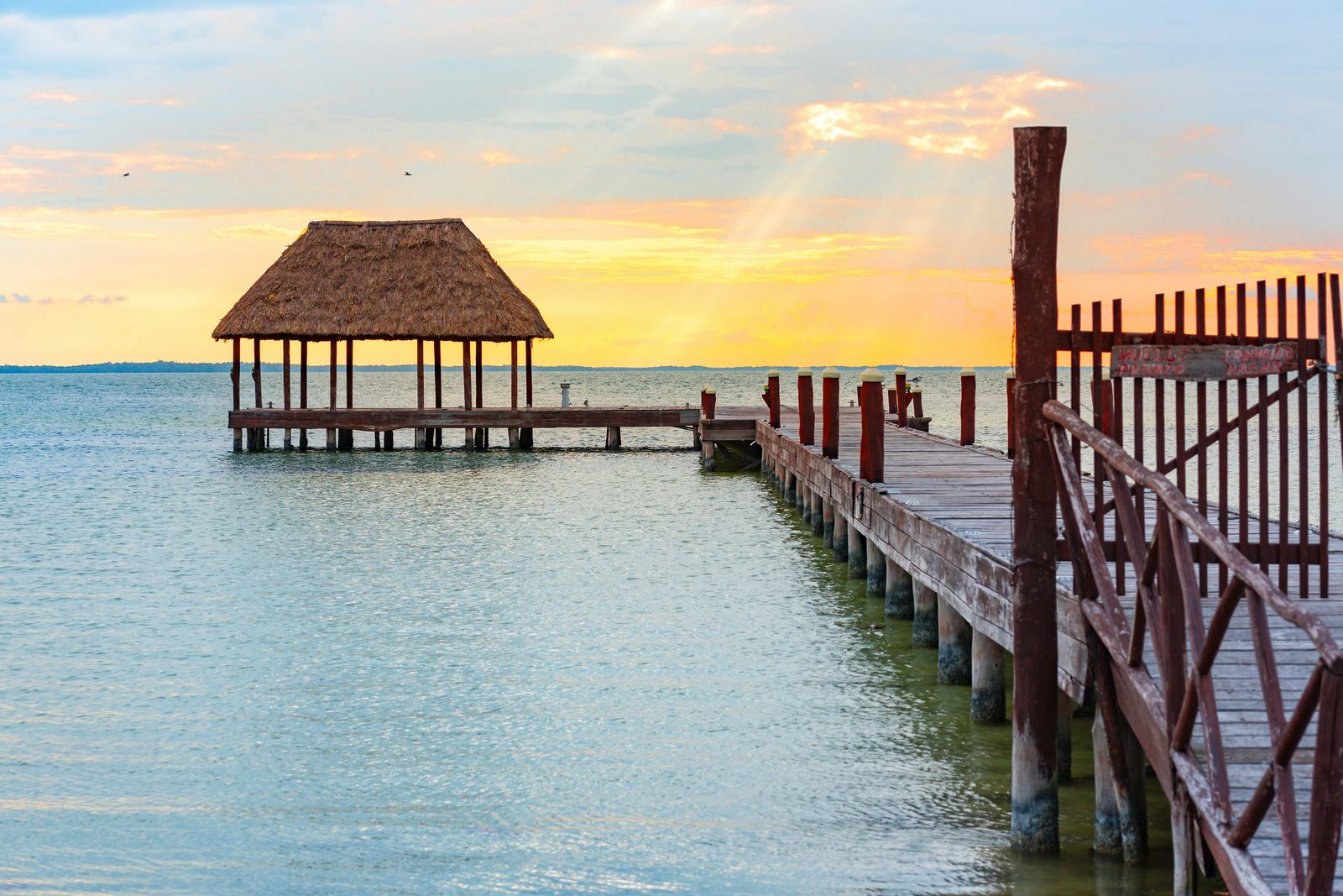 A pier running out over calm water under a sunset sky