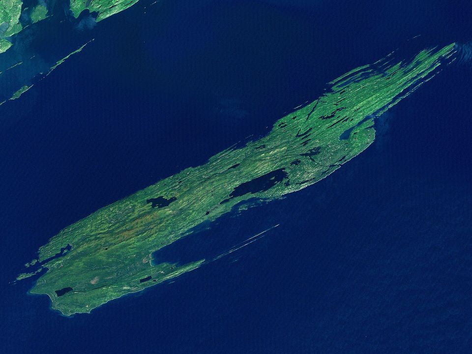 Satellite view of a narrow forested island with parallel ridges in a dark lake