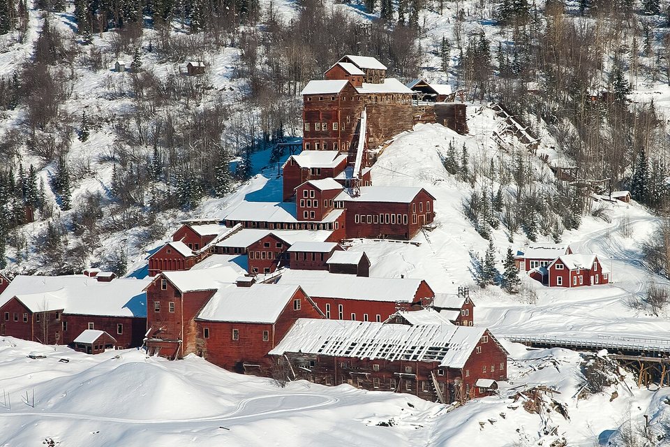 Red mill buildings with snow-covered roofs on a snowy, wooded hillside
