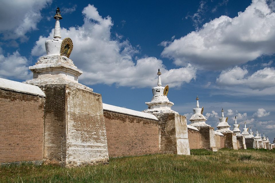 A long diagonal wall set with white stupas under a deep blue sky with big cumulus