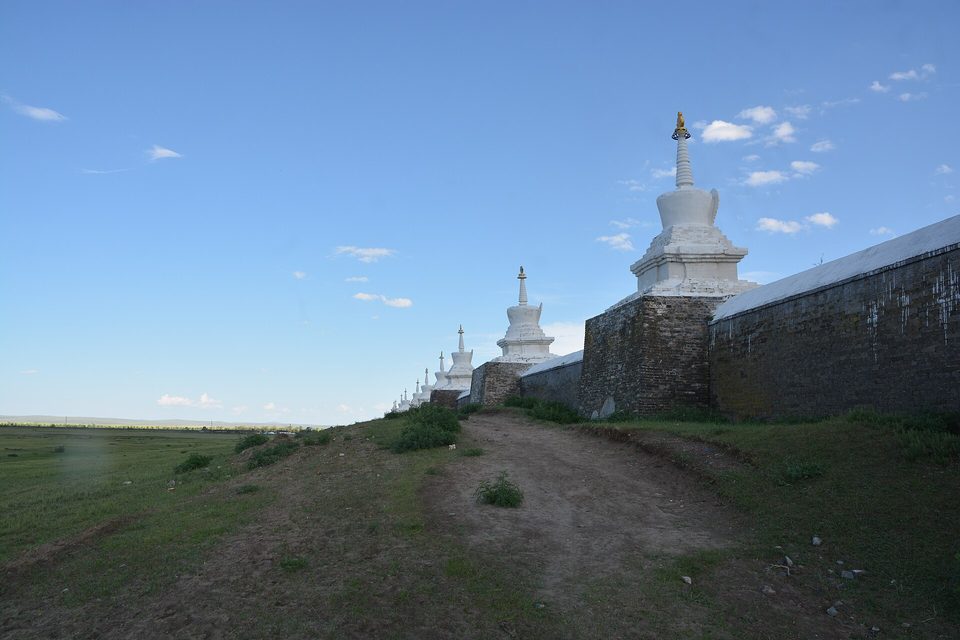 A line of white stupas along a monastery wall in evening light, open steppe stretching away to the left