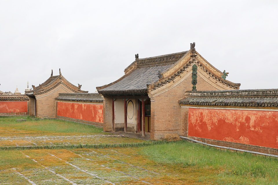 Red-plastered walls and a gate with carved roof ridges inside a monastery under a white sky