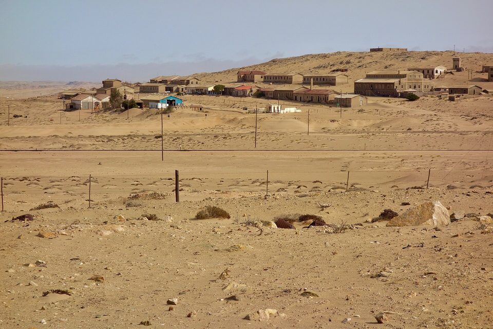 A straggle of low houses on a sand ridge above a flat desert plain crossed by a fence line and a pole line