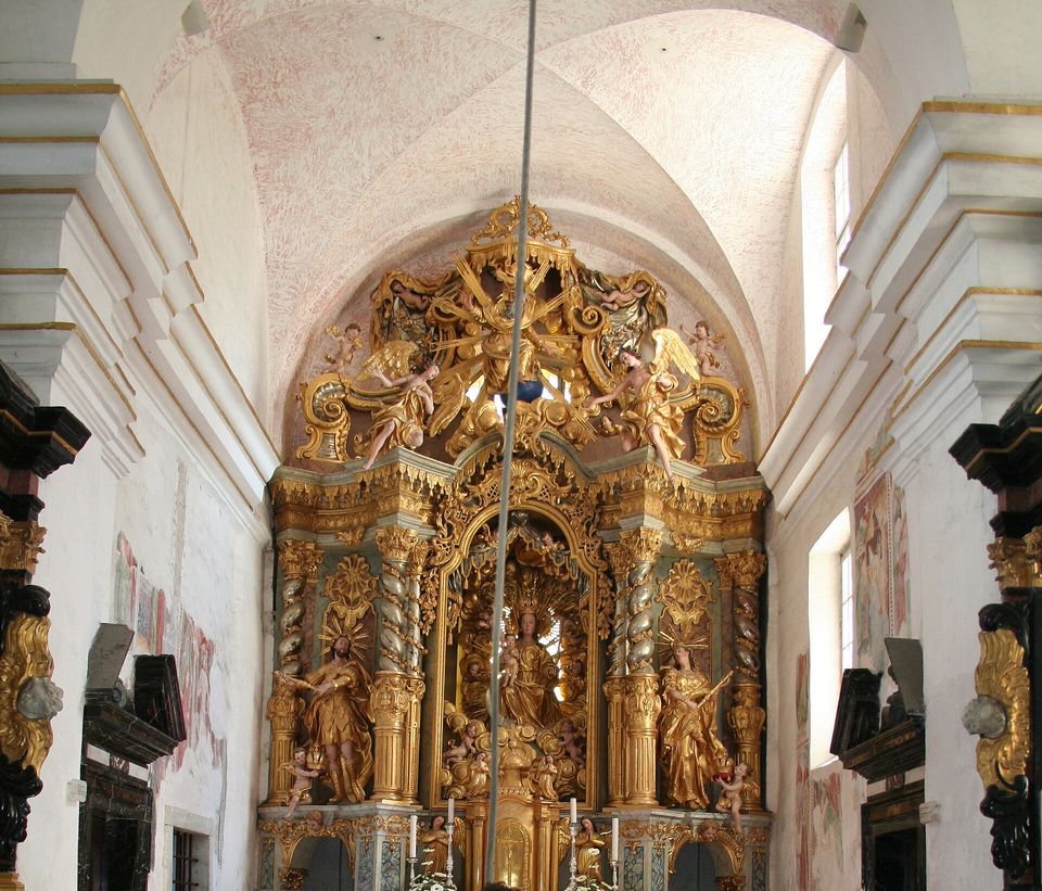 A bell rope hanging in front of a gilded baroque altar in a white vaulted church