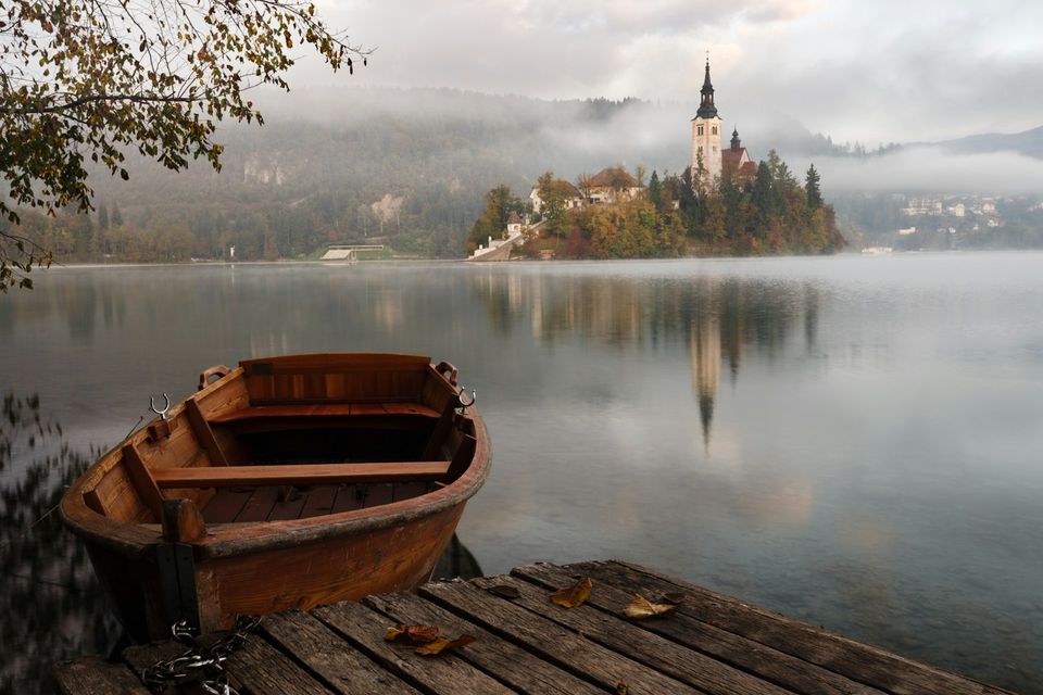 A wooden rowing boat at a jetty on still misty water, the island church faint beyond
