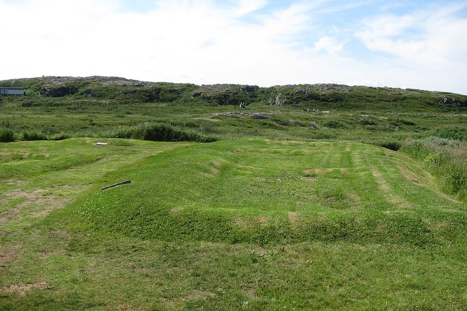 Low grassy ridges marking the outline of a long hall on open ground under a big sky