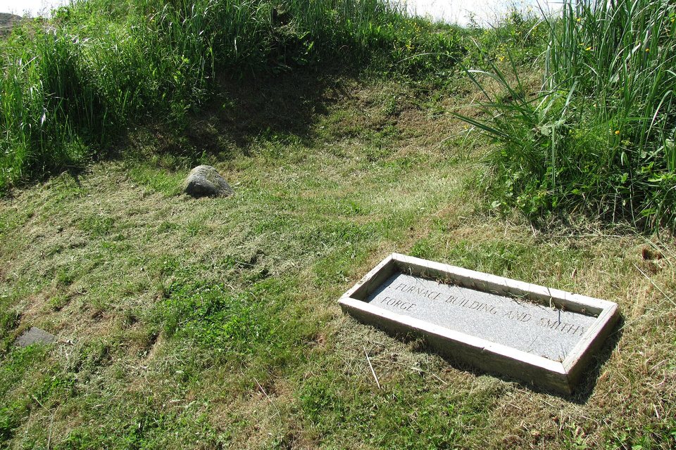 A grassy hollow with a stone plaque reading 'Furnace building and smithy forge'