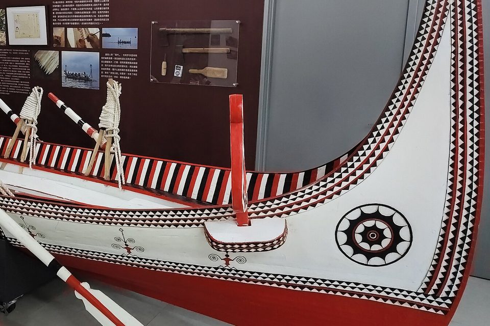 A large Tao plank boat on museum display, red, white and black, with the eye of the boat painted on its prow