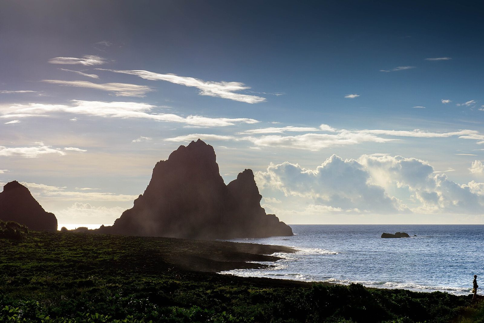 Volcanic sea stacks backlit at sunrise, spray on a black reef, a bright sea and towering cloud