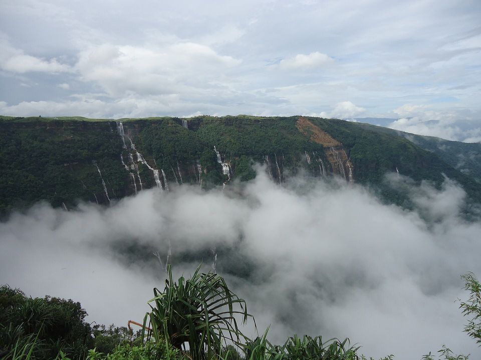 Several waterfalls streaming down a green cliff above a sea of cloud
