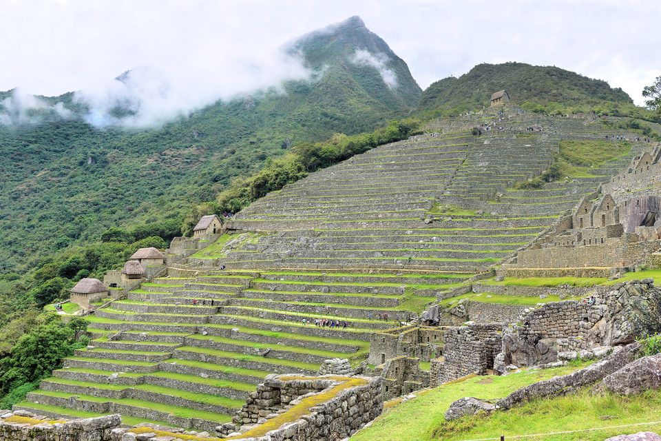 Steep green agricultural terraces stepping up a mountainside below a cloud-wrapped peak, small stone huts among the terraces