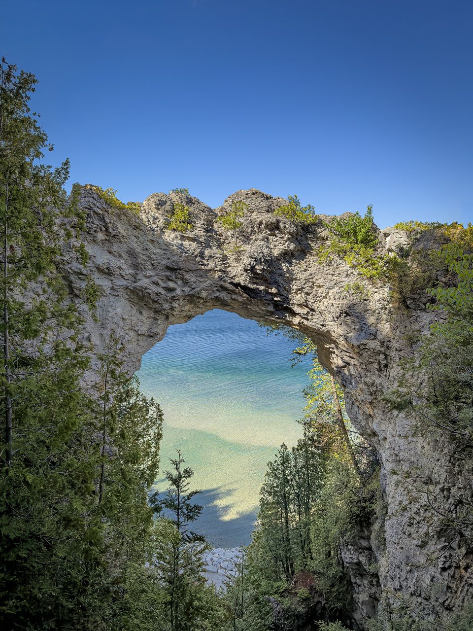 A natural limestone arch on a wooded bluff framing clear blue-green lake water