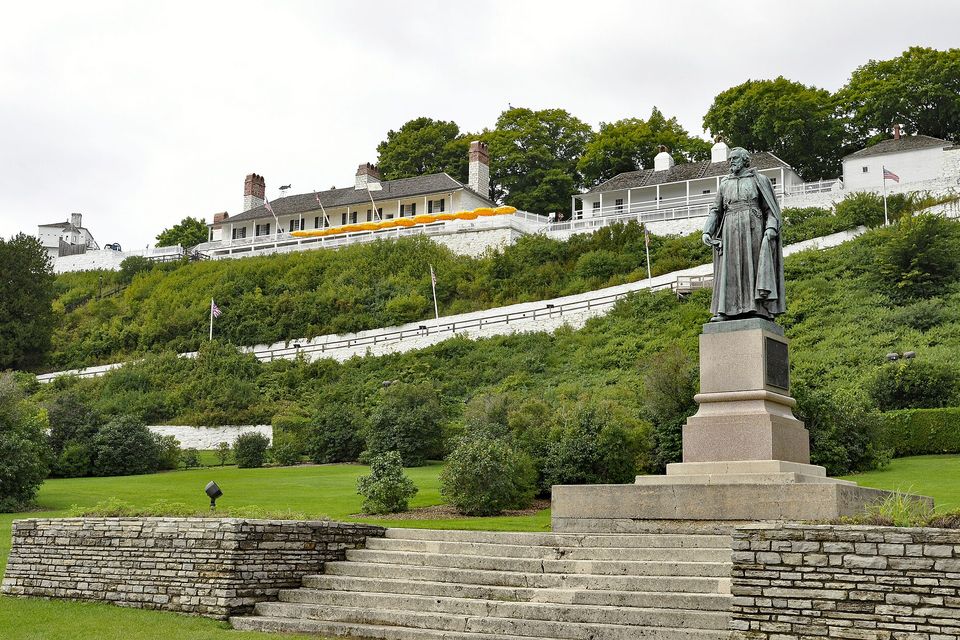 A white-walled fort on a green bluff above the harbour, a statue in the park in front, under a blue sky