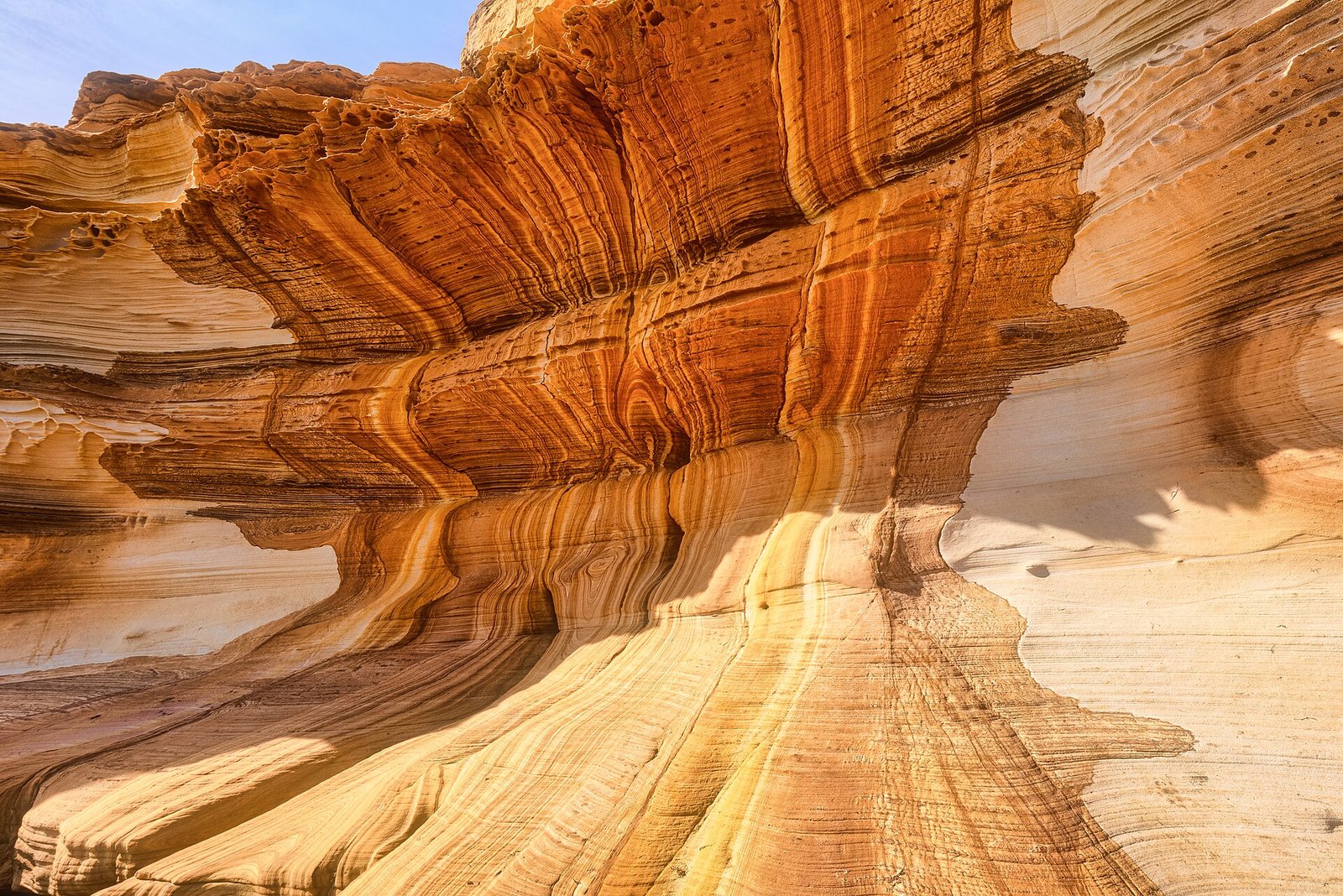 Swirling bands of orange, cream and rust in a sculpted sandstone overhang, with a strip of blue sky at the top