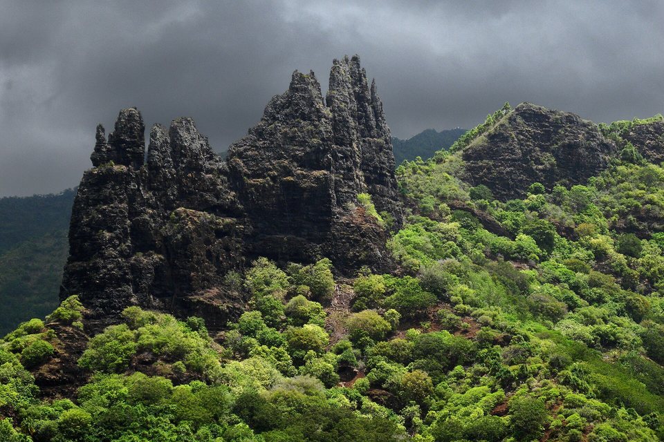 Jagged black basalt spires above a slope of bright green forest, under a dark storm sky