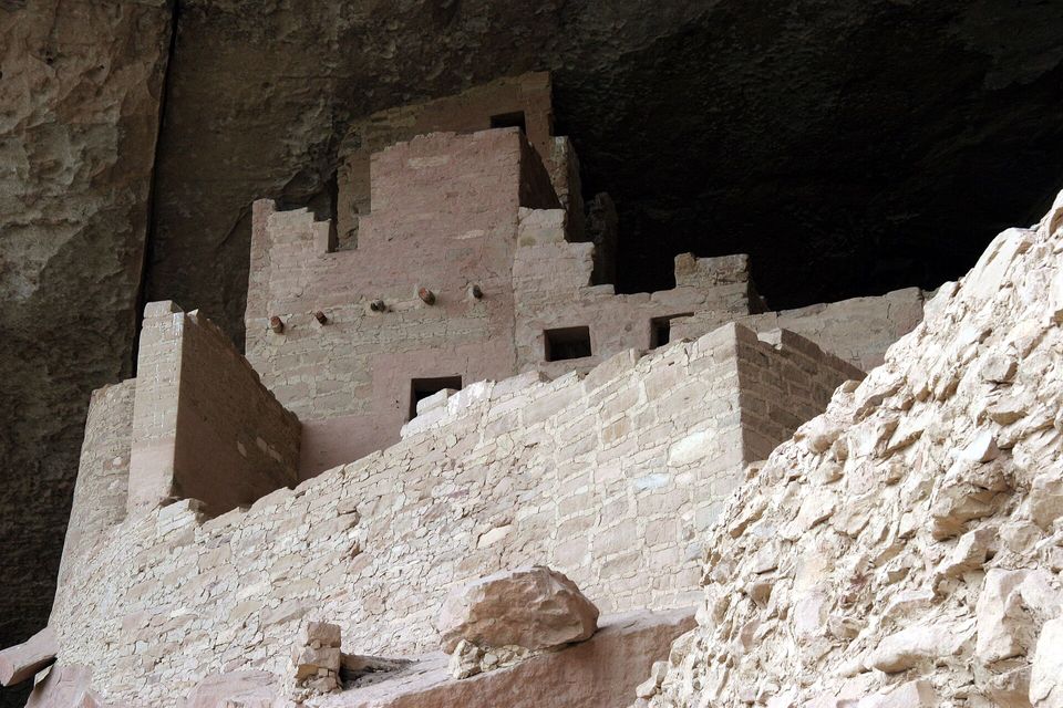 Close view of fitted stone walls and a tall stepped tower in deep shade under a rock overhang