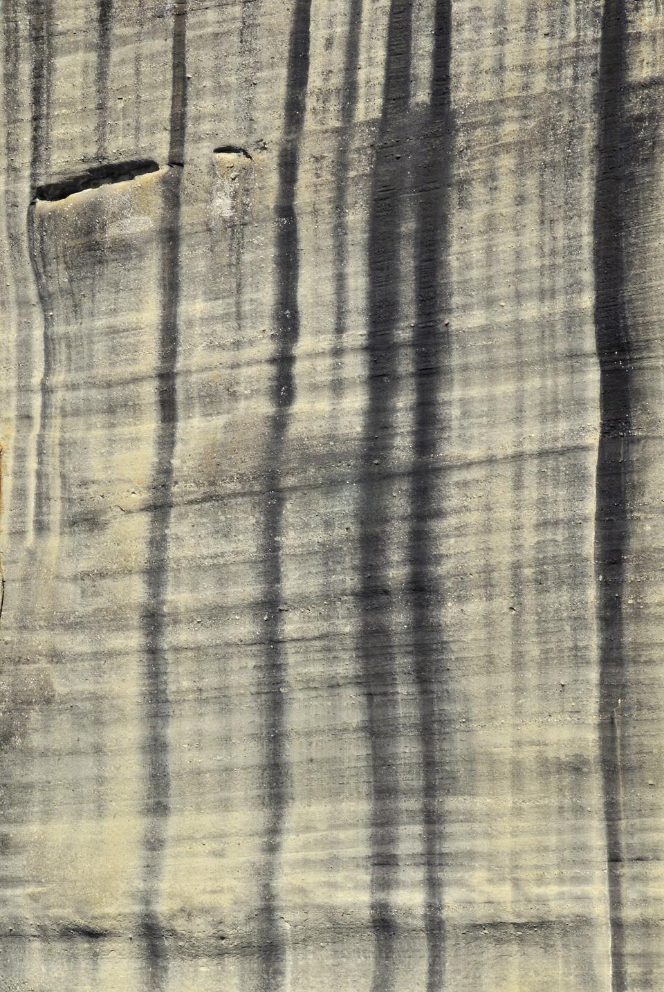 A close view of a pale layered rock face with dark vertical water streaks running down across horizontal bands