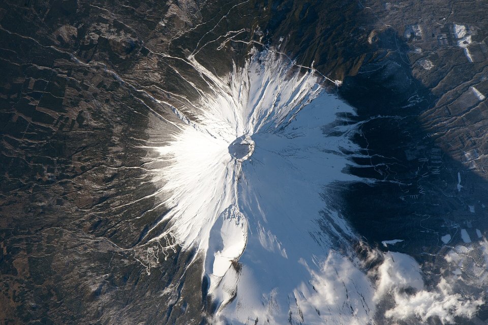 A snow-covered volcanic cone seen from above, a dark crater at its centre and gullies radiating down its flanks