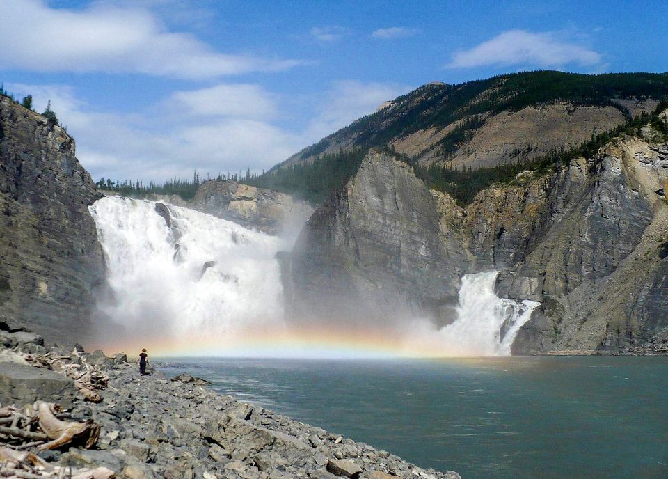 A wide waterfall split by a rock spire, with a rainbow in the spray