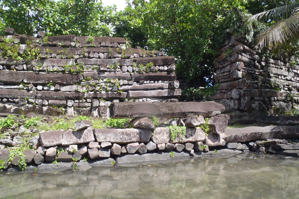 Close view of a basalt wall showing long prismatic columns laid lengthways and endways in alternating courses above a rubble footing at the water