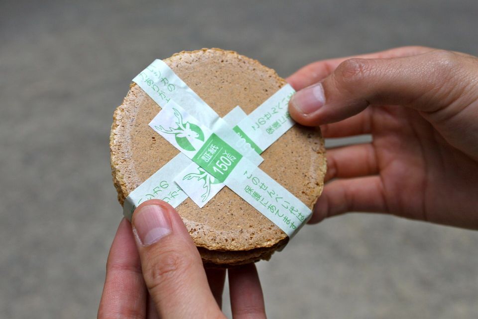 A stack of round brown crackers tied with a green and white paper band, held in two hands