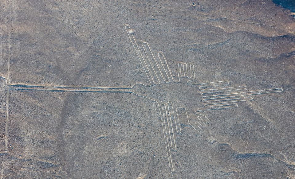 An aerial view of the hummingbird geoglyph: a long-billed bird drawn in one pale line on the stony brown desert, with straight lines crossing the ground around it