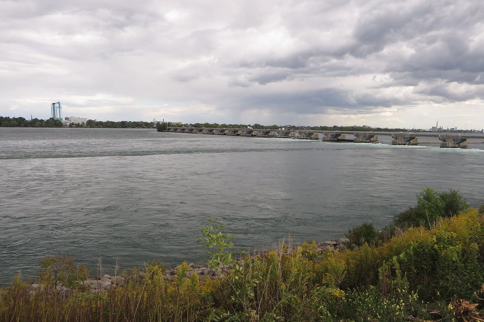 A long low line of concrete piers and gates stretching across a wide grey-green river under heavy cloud