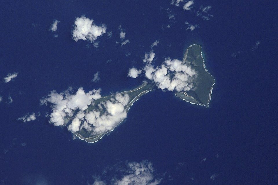 Two small islands joined by a reef, partly under cloud, in a deep-blue ocean seen from orbit