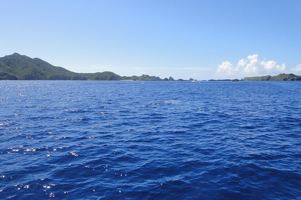 Low green hills and rocky islets on the horizon across deep-blue open sea