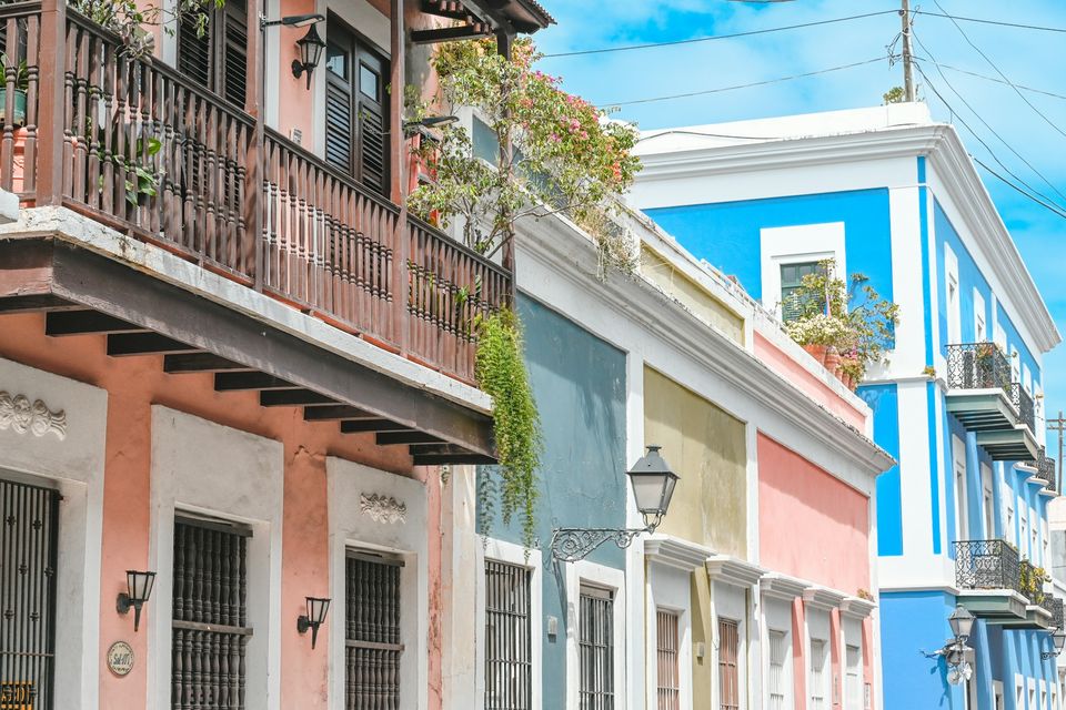 A row of pastel buildings with wrought-iron balconies, hanging plants and lamps
