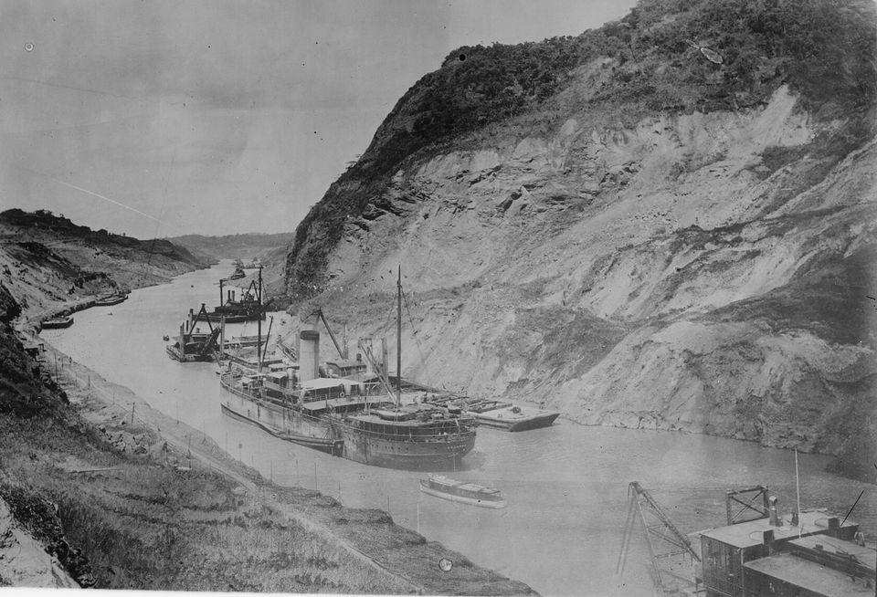 A black and white photograph of a wide cut through a bare hillside, with steamers, dredges and a launch on the water below