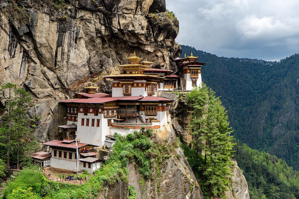 White temple buildings clinging to a sheer cliff above forest
