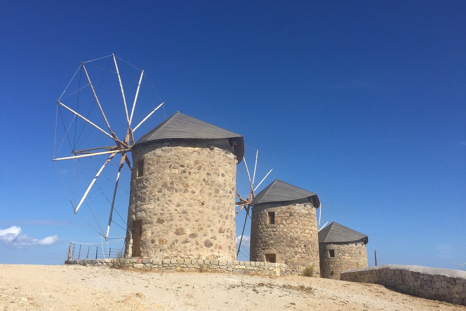 Three round stone windmills with conical grey roofs and wooden sails on a bare hilltop against a deep blue sky