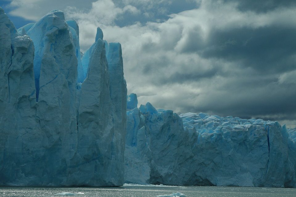 Tall jagged spires of pale blue ice rising from water under dark storm clouds