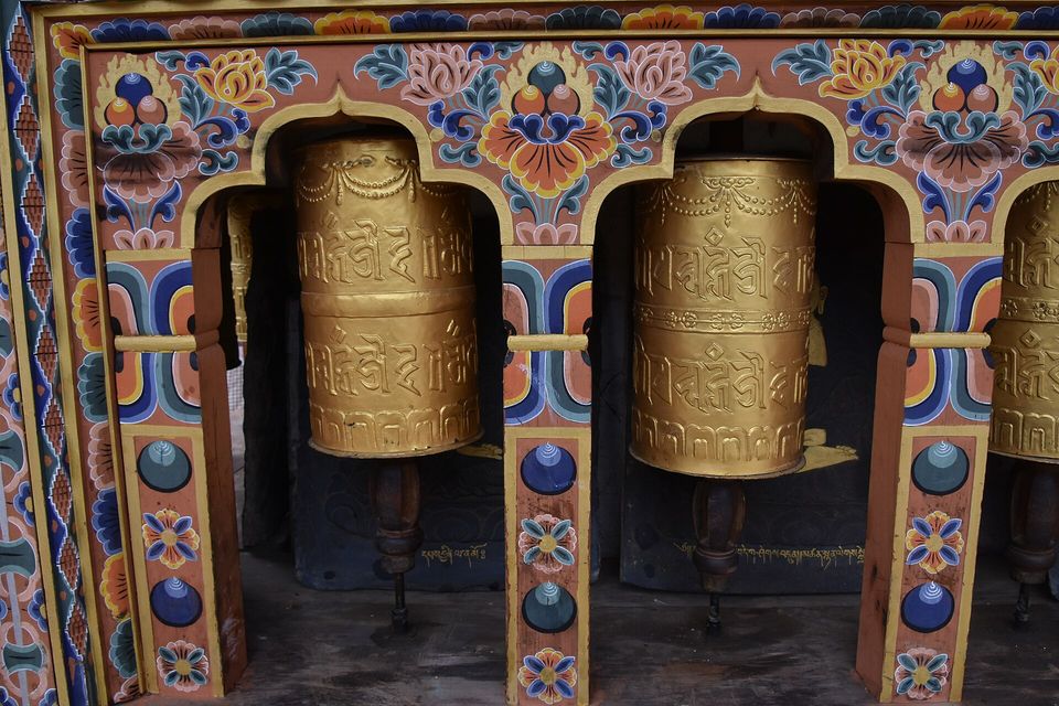 Two golden prayer wheels embossed with Tibetan script turn in arched niches painted with lotus flowers in blue, orange and cream