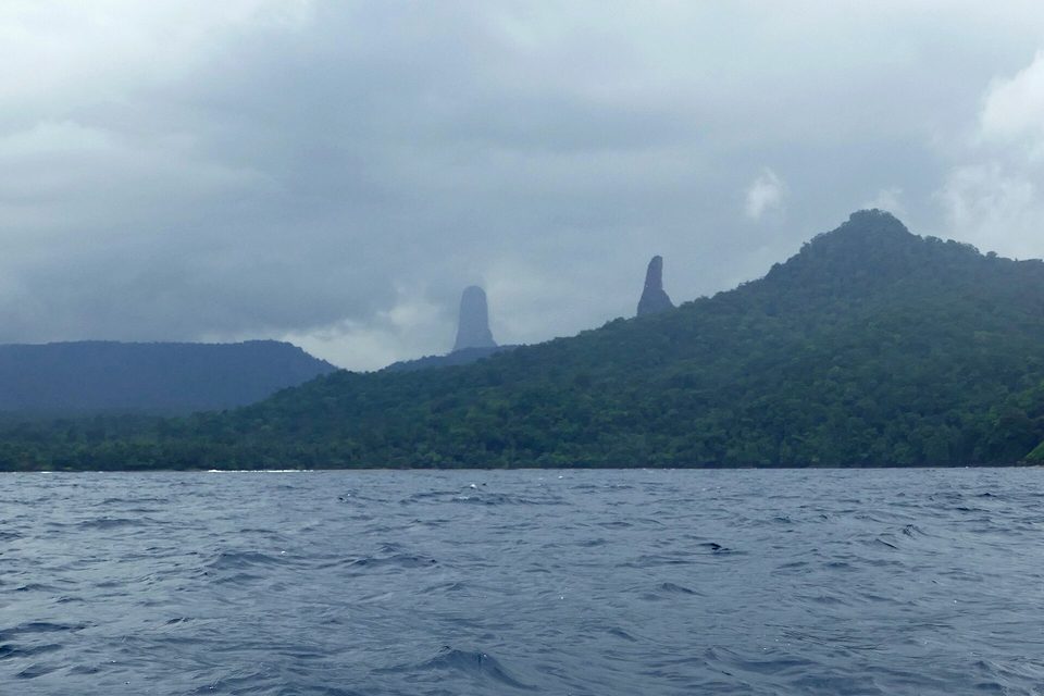Two rock needles in cloud above a green coast, seen from a boat on the sea