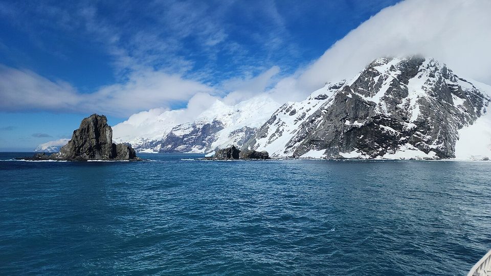 A narrow spit between a glacier and sea stacks with snowy peaks behind