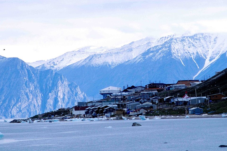 A small settlement on a slope below snowy peaks, with small floes along the shore