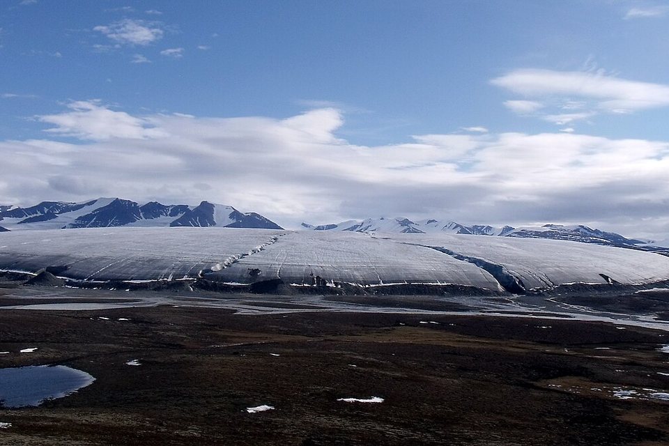 A wide lobe of glacier ice spreading onto tundra ponds under a blue sky