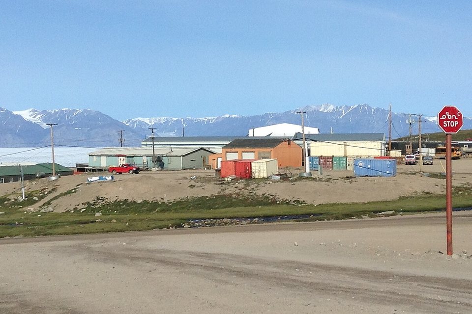 A stop sign with Inuktitut and English text beside a road, with mountains behind